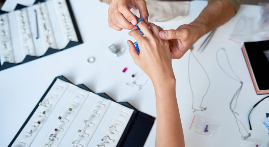 Closeup of man checking ring size of elegant female hand in jewelry shop