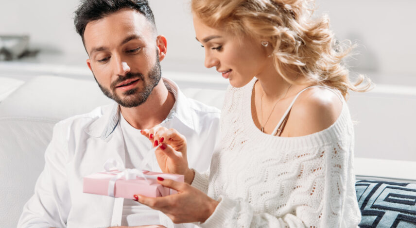 Charming girl sitting on sofa with boyfriend and holding gift